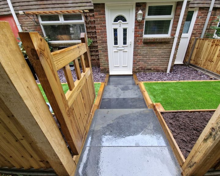 A front garden that has been landscaped with new artificial grass, wooden fences and a gate.