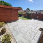 A garden that has been landscaped using a new grey patio and a wooden garden room.