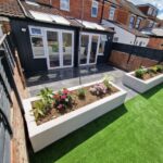A garden with a grey patio that has had new artificial grass installed and new flower beds.