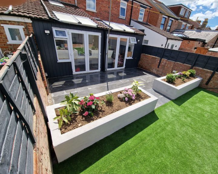 A garden with a grey patio that has had new artificial grass installed and new flower beds.