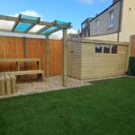 Well-kept backyard with artificial grass, a wooden pergola, bench, shed, and fenced boundaries.