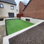 A newly renovated urban backyard with synthetic green grass and white brick borders between residential buildings.