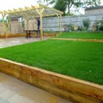 A landscaped backyard with artificial grass, wooden decking, and a pergola.