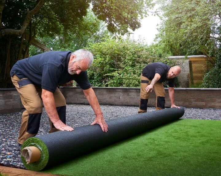 Two landscape gardeners installing new artificial grass in a garden